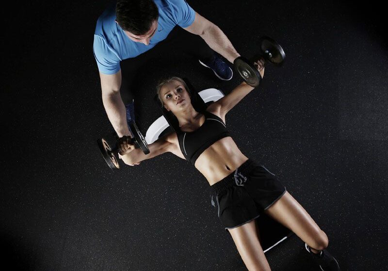 A man helping a woman do exercises with dumbbells.